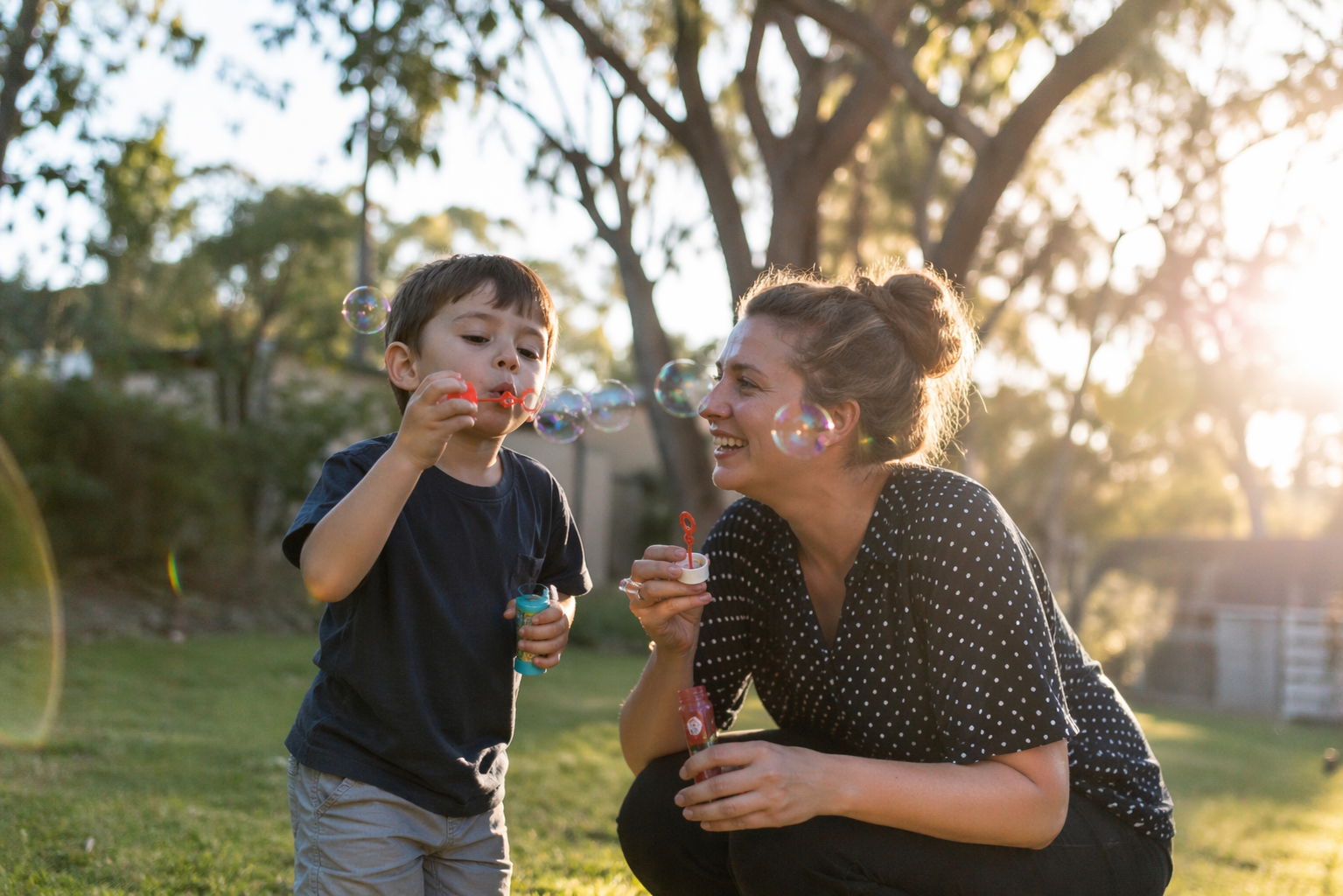 Speech pathologist and a laughing young boy blowing bubbles outdoors at golden hour
